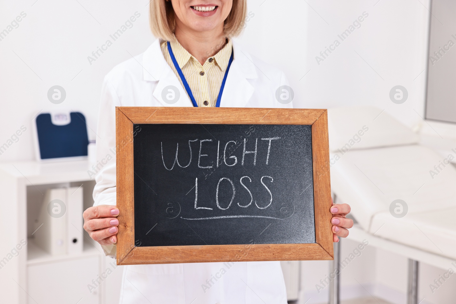 Photo of Happy nutritionist holding small blackboard with words Weight loss in clinic, closeup