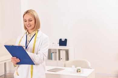 Photo of Weight loss. Happy nutritionist with clipboard in clinic, space for text