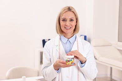 Photo of Happy nutritionist with bottle of weight loss pills in clinic. Space for text