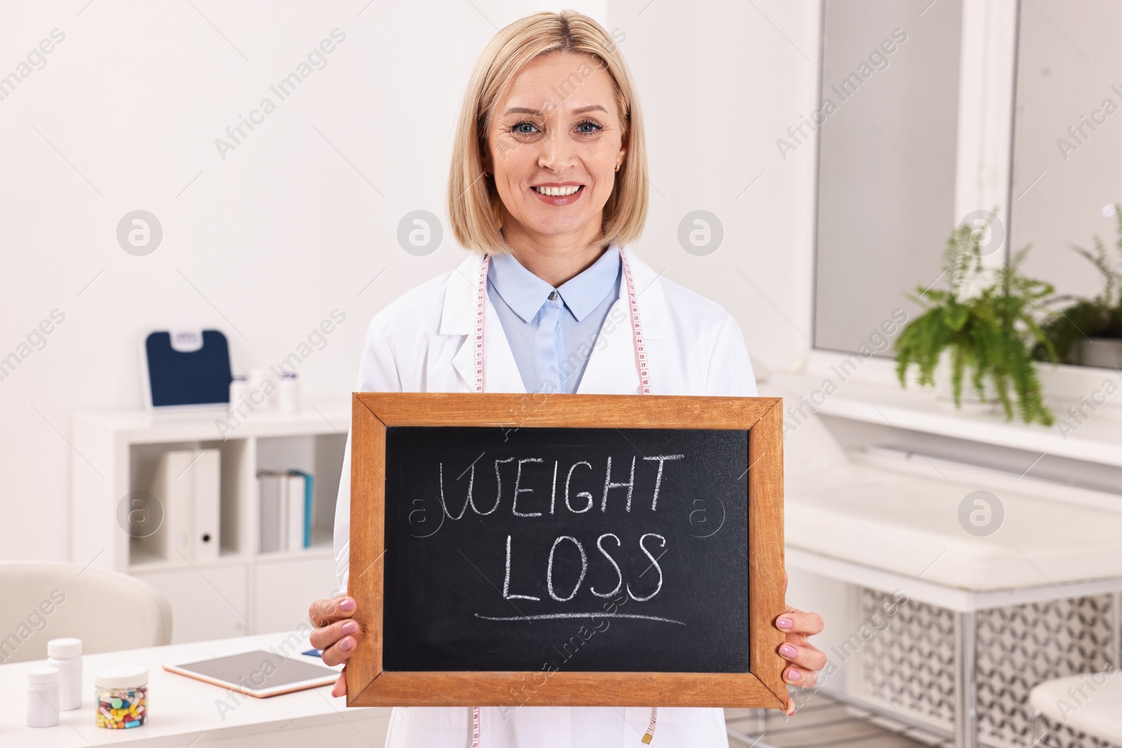 Photo of Happy nutritionist holding small blackboard with words Weight loss in clinic