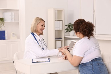 Photo of Weight loss. Smiling nutritionist with tablet consulting patient at table in clinic