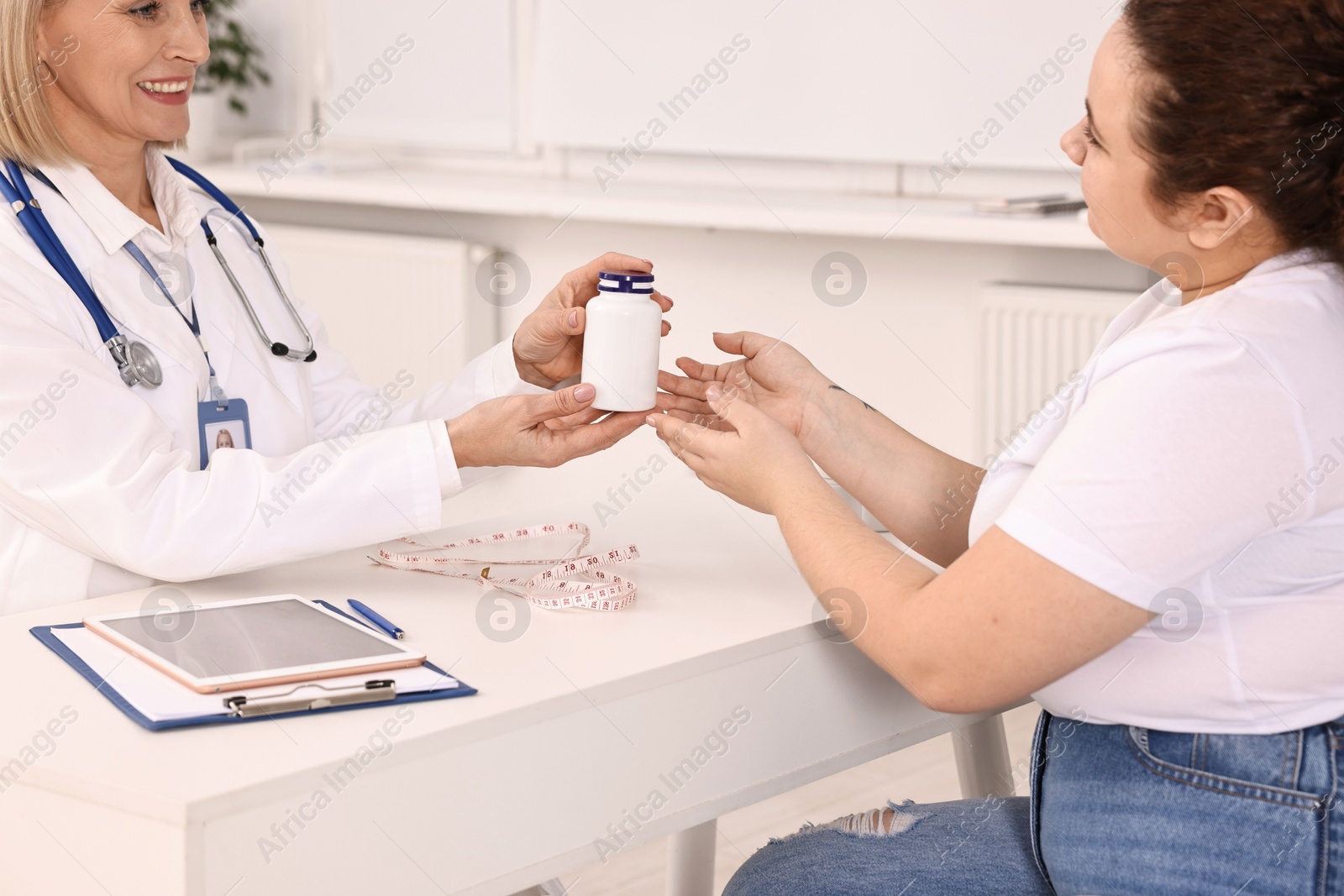 Photo of Weight loss. Smiling nutritionist giving medical bottle with pills to patient at table in clinic