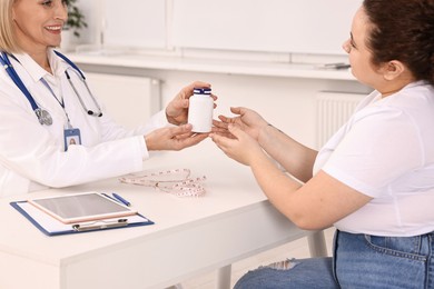 Photo of Weight loss. Smiling nutritionist giving medical bottle with pills to patient at table in clinic