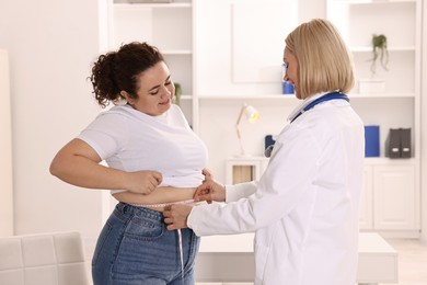 Photo of Happy woman lost weight. Smiling nutritionist measuring patient's waist with tape in clinic