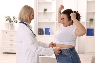 Photo of Happy woman lost weight. Smiling nutritionist measuring patient's waist with tape in clinic