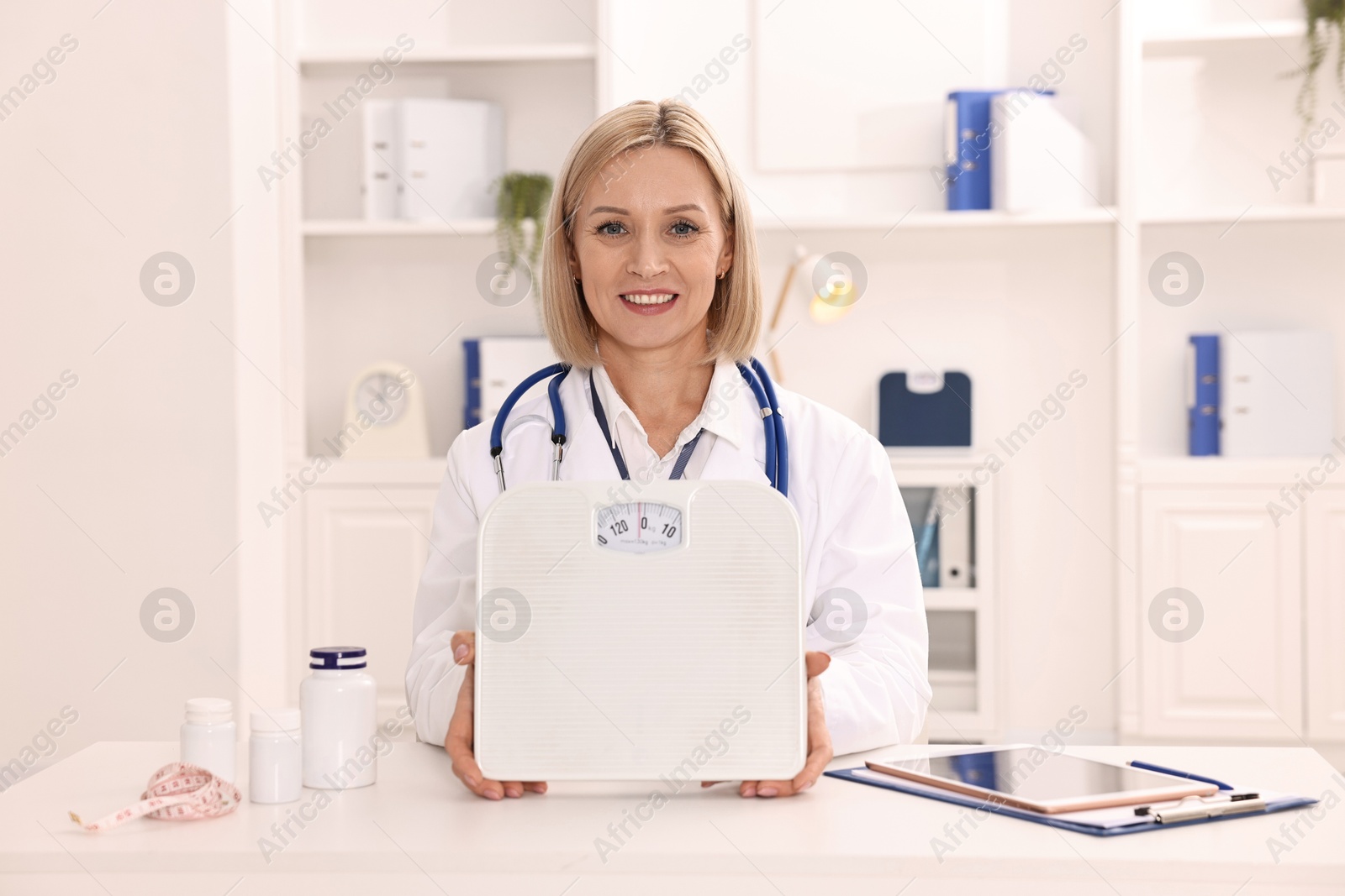 Photo of Weight loss. Smiling nutritionist with scales at table in clinic