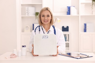 Photo of Weight loss. Smiling nutritionist with scales at table in clinic