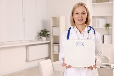 Photo of Weight loss. Smiling nutritionist with stethoscope and scales in clinic. Space for text