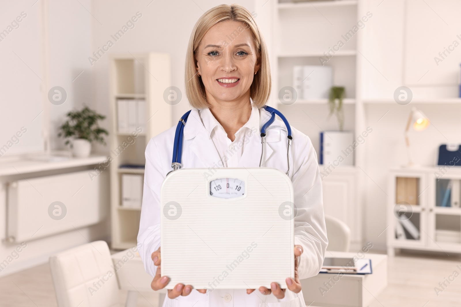 Photo of Weight loss. Smiling nutritionist with stethoscope and scales in clinic