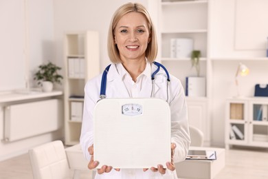 Photo of Weight loss. Smiling nutritionist with stethoscope and scales in clinic