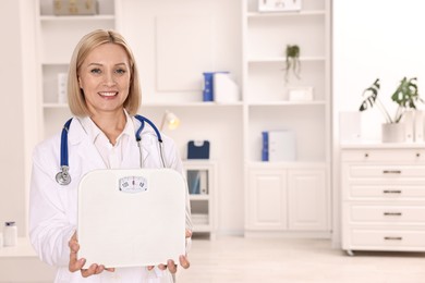 Photo of Weight loss. Smiling nutritionist with stethoscope and scales in clinic. Space for text