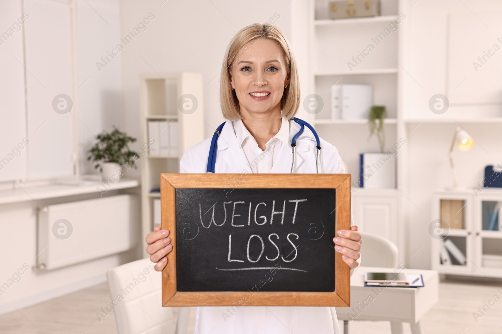 Photo of Happy nutritionist holding small blackboard with words Weight loss in clinic