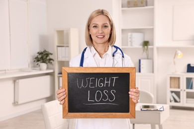 Photo of Happy nutritionist holding small blackboard with words Weight loss in clinic