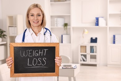 Photo of Happy nutritionist holding small blackboard with words Weight loss in clinic. Space for text