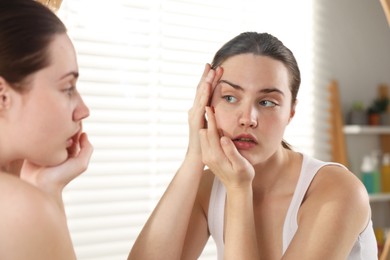 Photo of Young woman putting in red color contact lens near mirror indoors