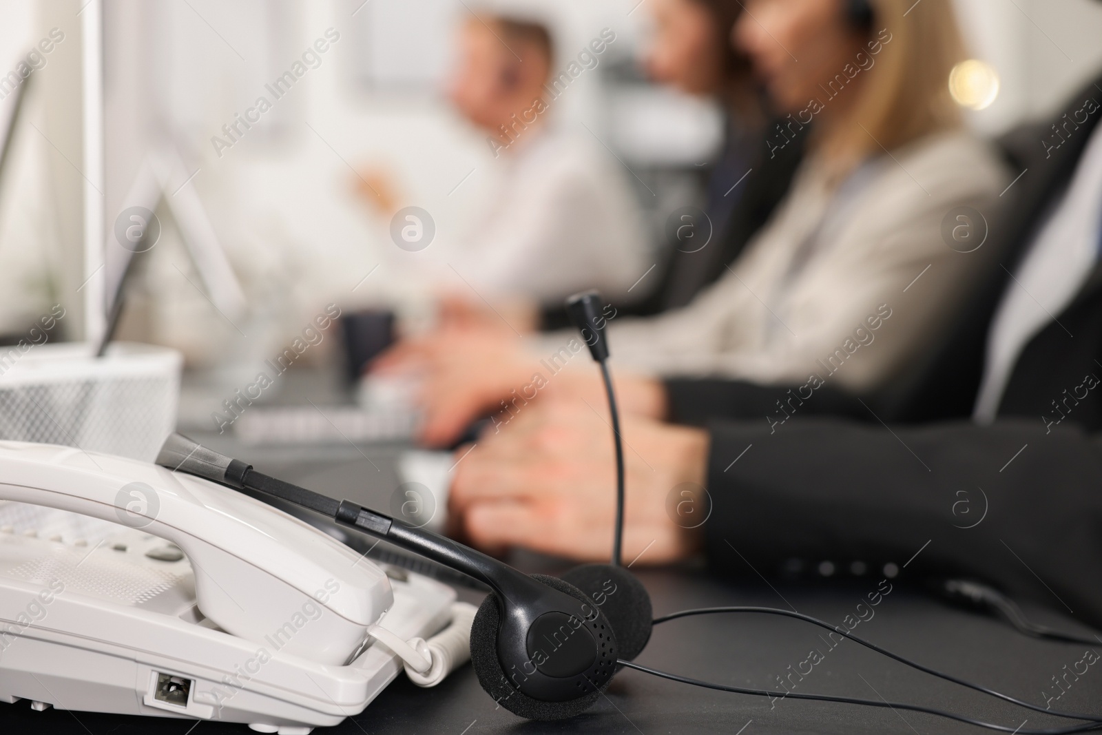 Photo of Technical support call center. Team of operators working at table in office, focus on phone and headset