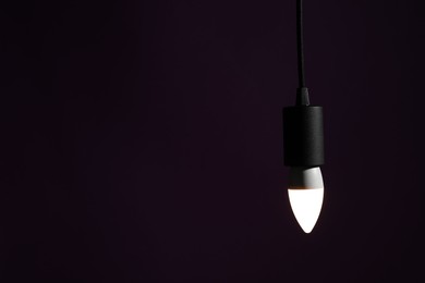 Photo of Glowing light bulb hanging on dark purple background. Space for text