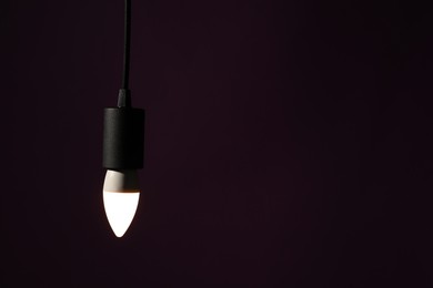 Photo of Glowing light bulb hanging on dark purple background. Space for text