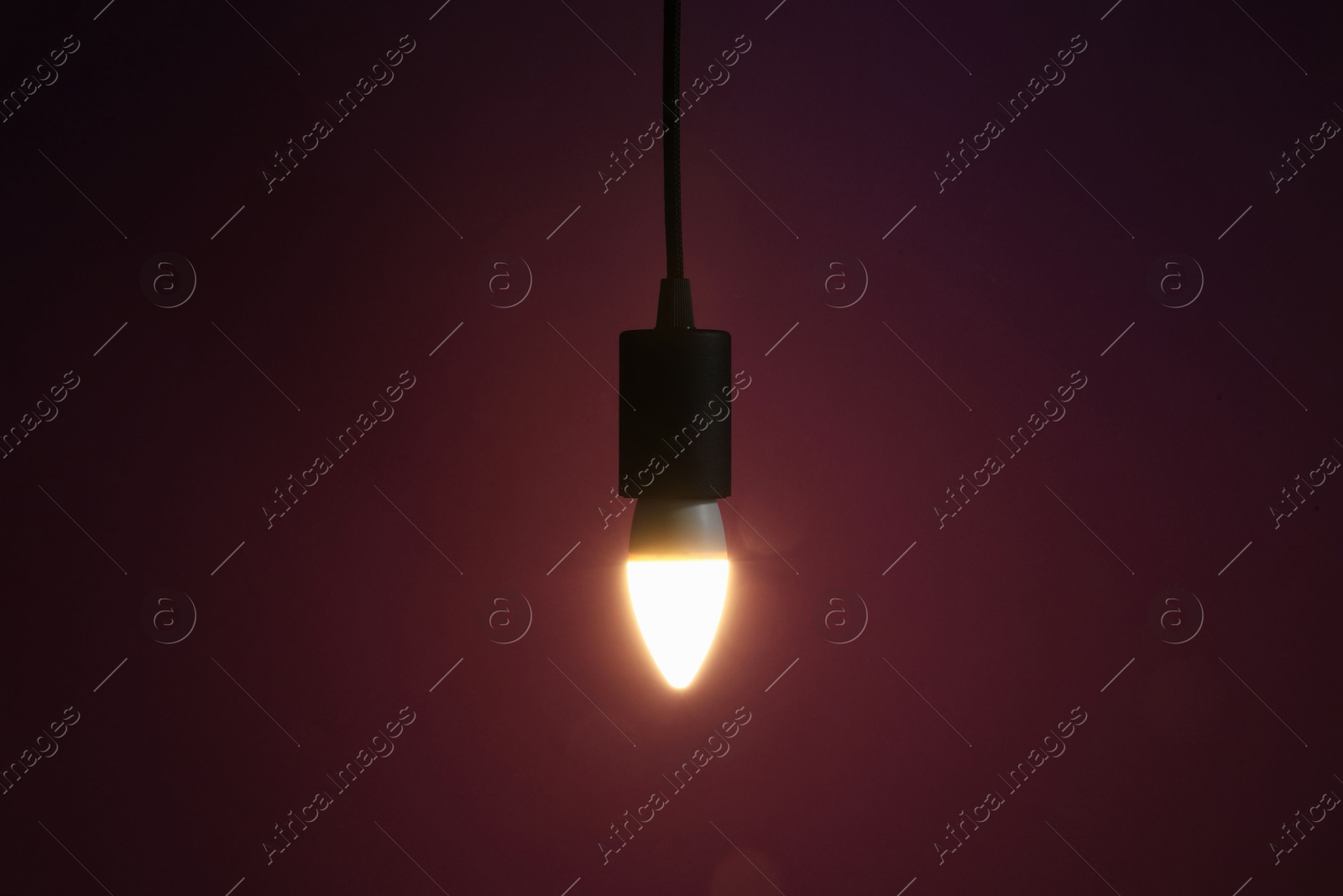 Photo of Glowing light bulb hanging on dark purple background