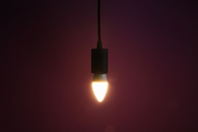 Photo of Glowing light bulb hanging on dark purple background