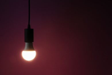 Photo of Glowing light bulb hanging on dark purple background. Space for text