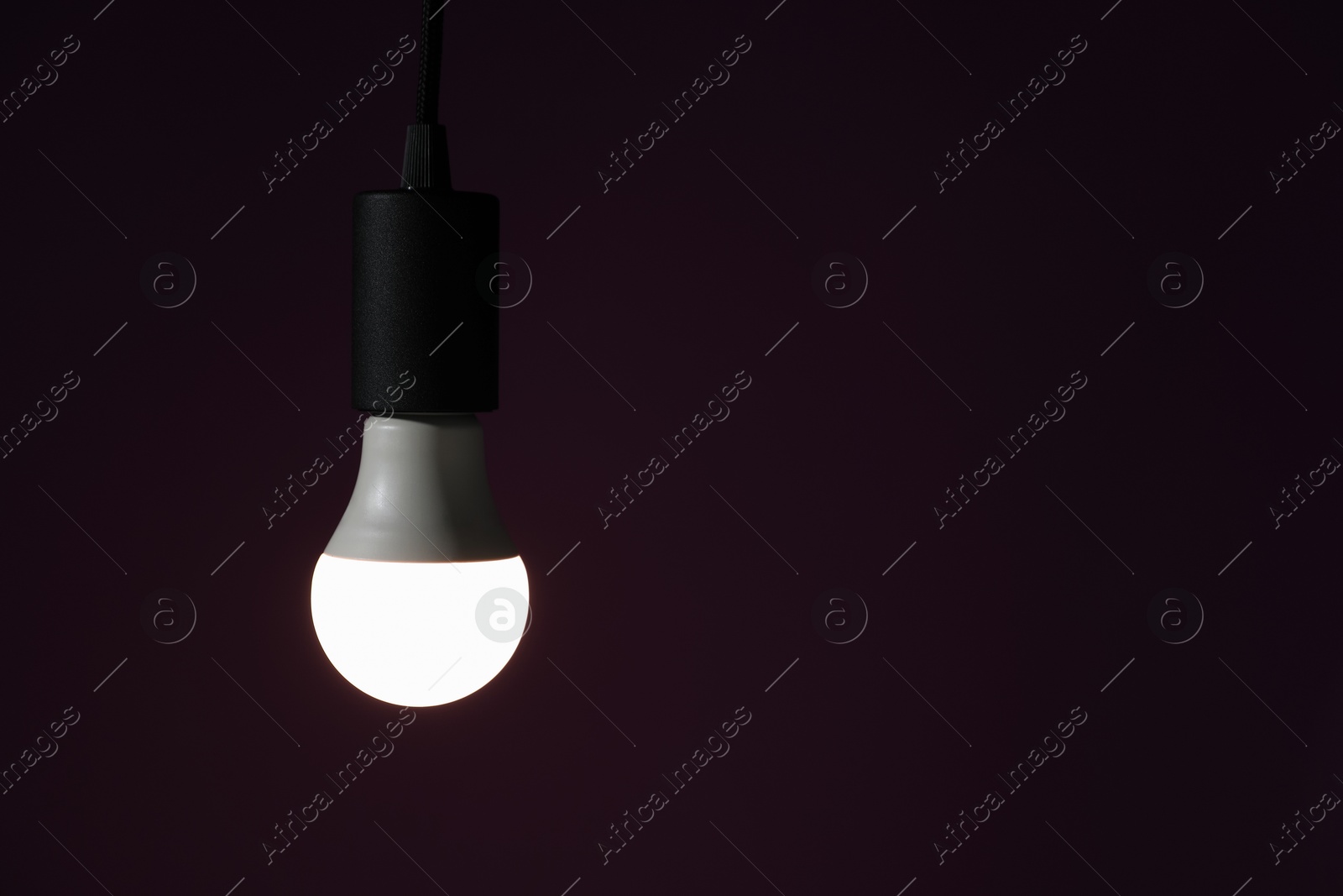 Photo of Glowing light bulb hanging on dark purple background. Space for text