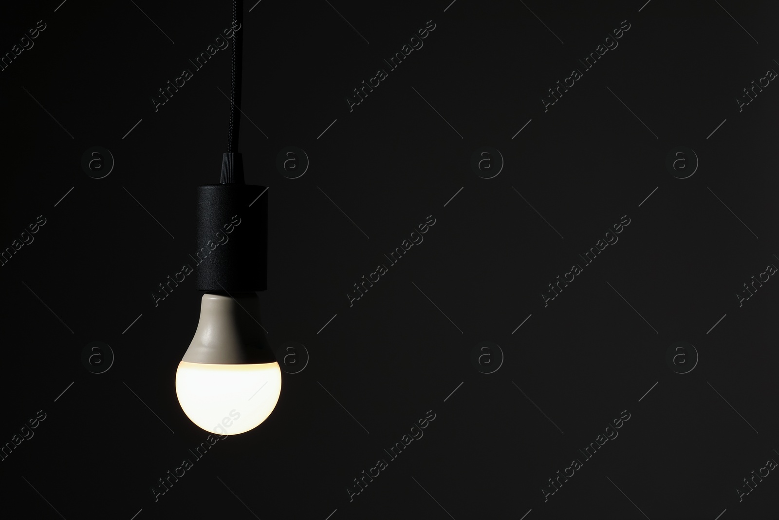 Photo of Glowing light bulb hanging on dark background. Space for text