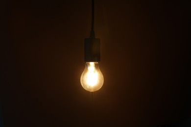 Photo of Glowing light bulb hanging on dark background