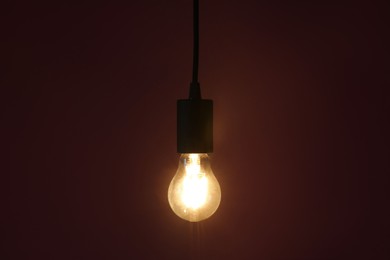 Photo of Glowing light bulb hanging on color background