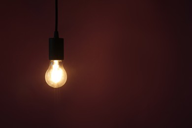 Photo of Glowing light bulb hanging on color background, space for text