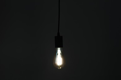 Photo of Glowing light bulb hanging on dark background