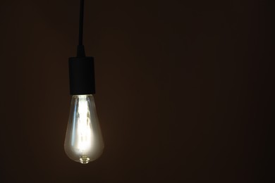 Photo of Glowing light bulb hanging on dark background. Space for text