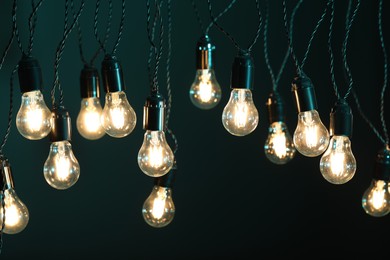 Photo of Glowing light bulbs hanging on color background, closeup