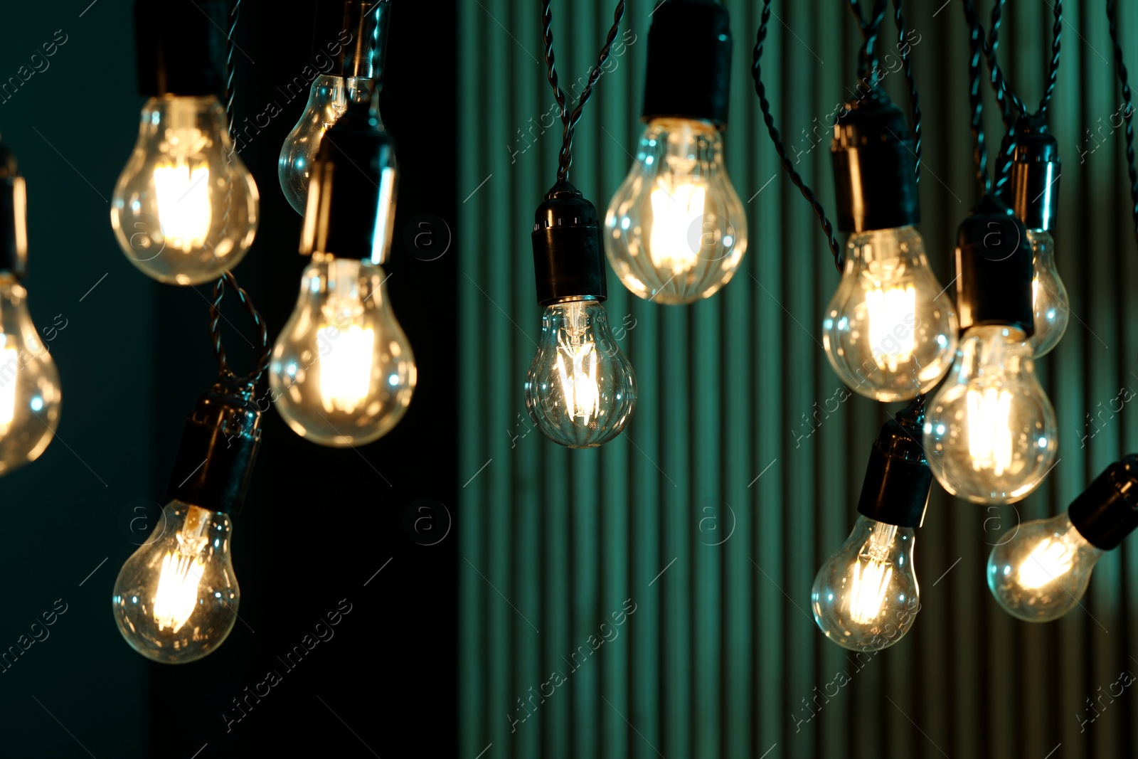 Photo of Glowing light bulbs hanging on color background, closeup