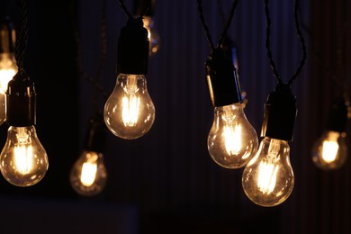 Photo of Glowing light bulbs hanging indoors, closeup view