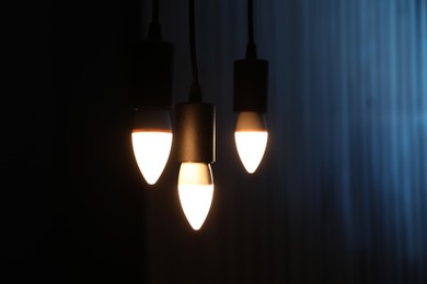 Photo of Glowing light bulbs hanging against color background, closeup