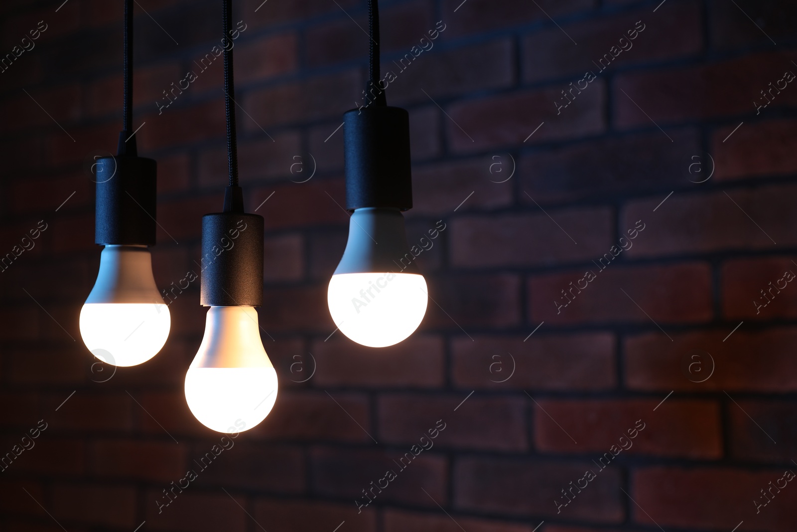 Photo of Glowing light bulbs hanging against brick wall, space for text