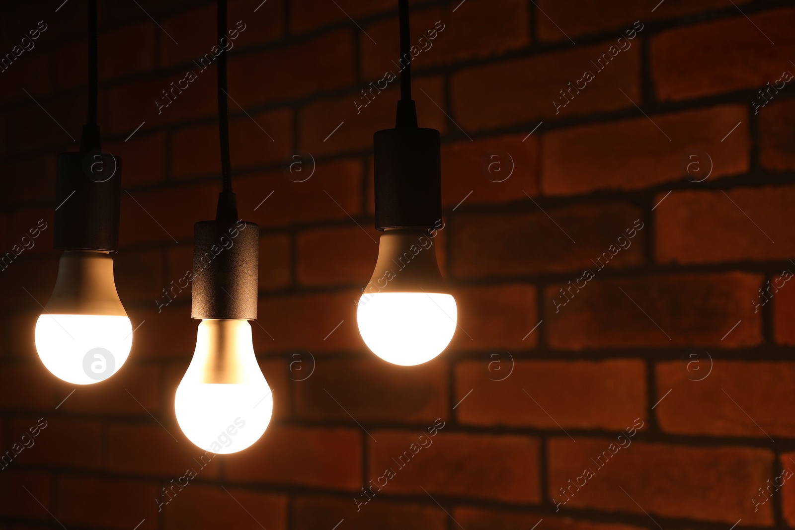 Photo of Glowing light bulbs hanging against brick wall, space for text