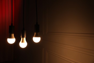 Photo of Glowing light bulbs hanging indoors, space for text