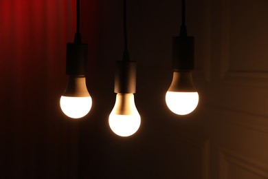 Photo of Glowing light bulbs hanging indoors, closeup view