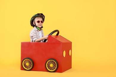 Photo of Little boy driving car made of cardboard on yellow background. Space for text