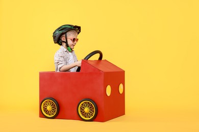 Photo of Little boy driving car made of cardboard on yellow background. Space for text