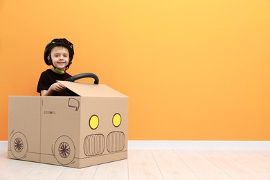 Photo of Little boy driving car made of cardboard against orange wall. Space for text