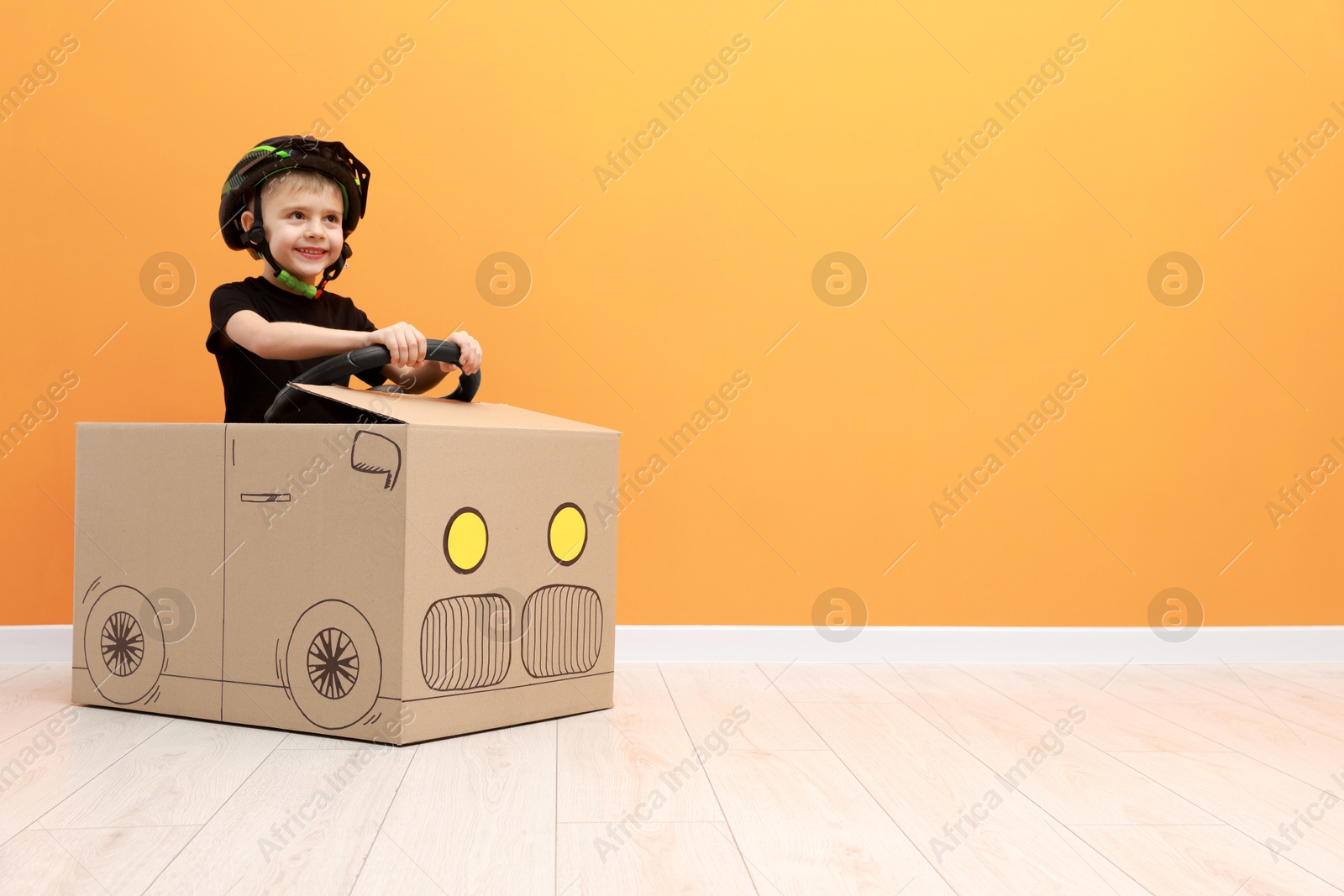 Photo of Little boy driving car made of cardboard against orange wall. Space for text