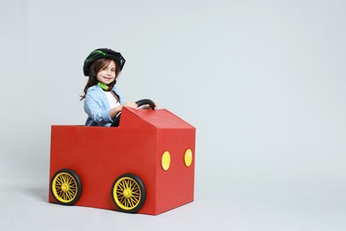 Photo of Little girl driving car made with cardboard on light background. Space for text