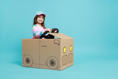 Photo of Little girl driving car made with cardboard on light blue background. Space for text