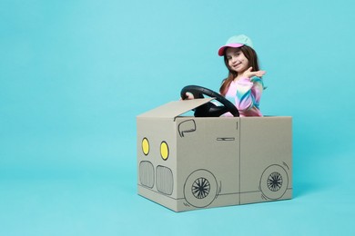 Photo of Little girl waving while driving car made with cardboard on light blue background. Space for text