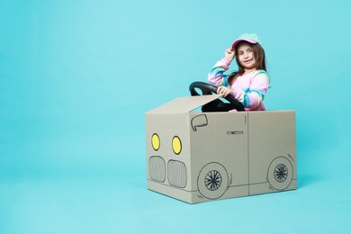 Photo of Little girl driving car made with cardboard on light blue background. Space for text