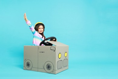 Photo of Little girl waving while driving car made with cardboard on light blue background. Space for text