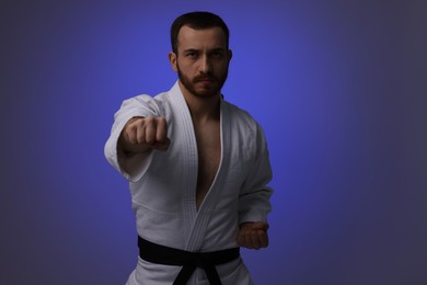 Photo of Man in uniform practicing karate on dark purple background